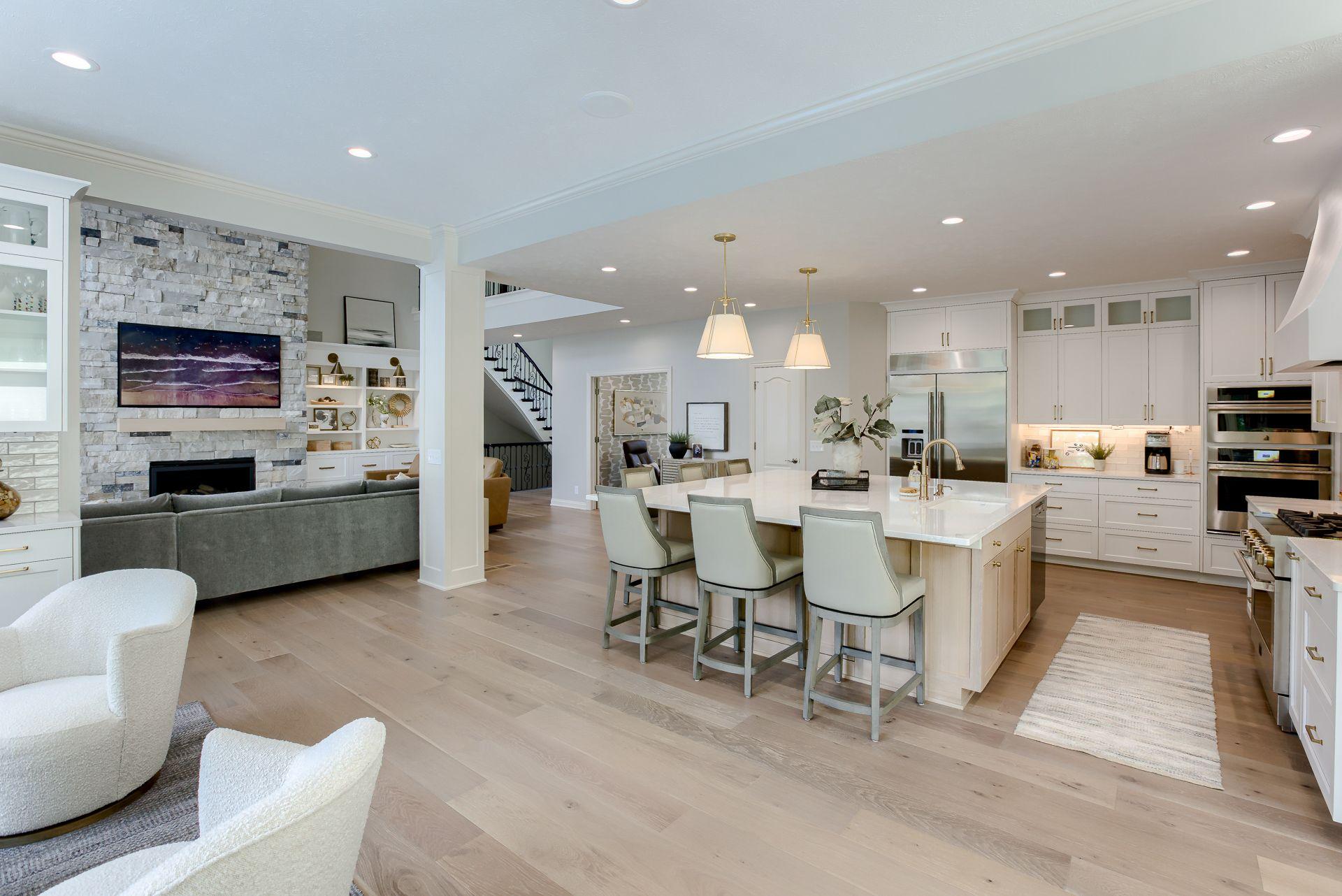 Modern open-plan living room and kitchen with white cabinets, large island, and stone fireplace.