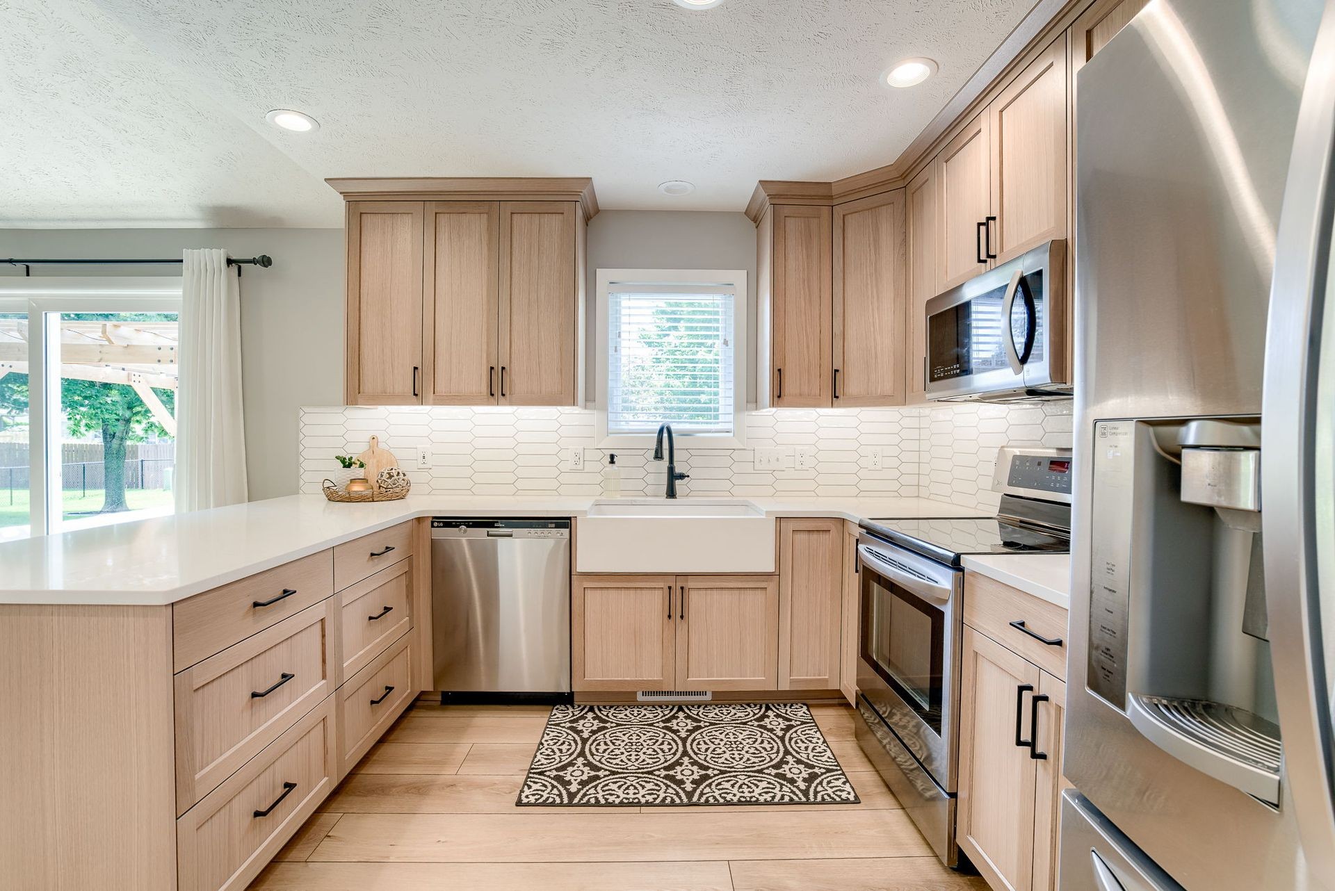 Modern kitchen with light wood cabinets, stainless steel appliances, and a farmhouse sink.