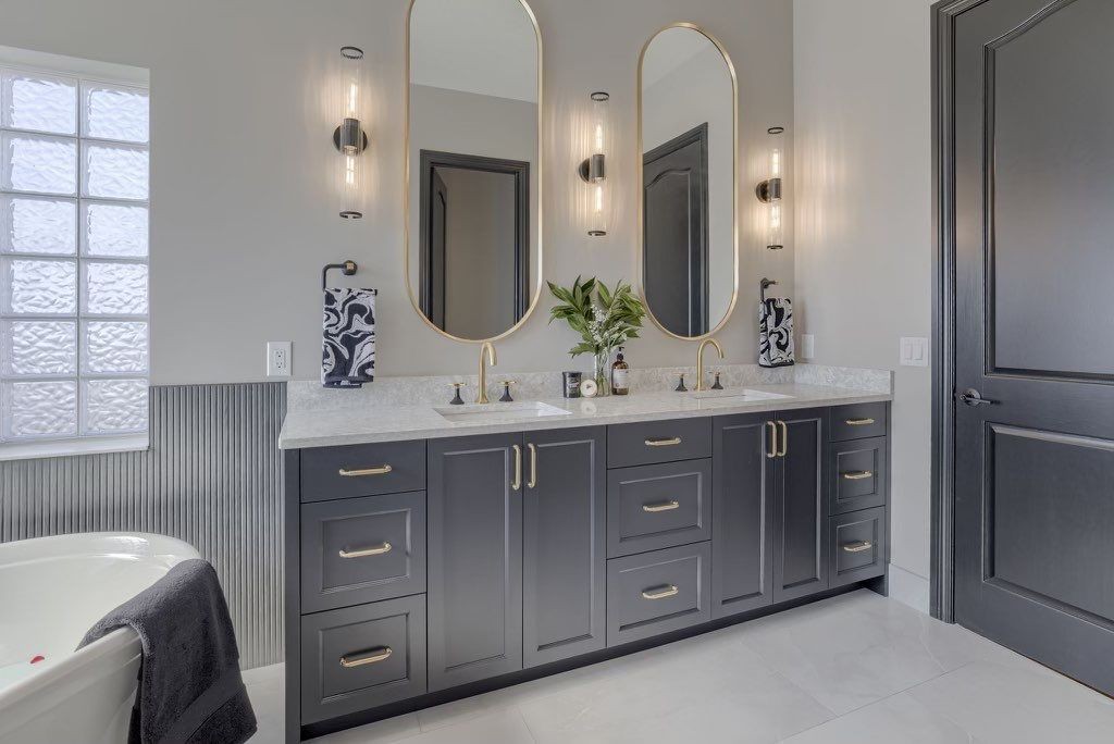 Modern bathroom with dual sinks, black cabinets, gold fixtures, and tall mirrors.