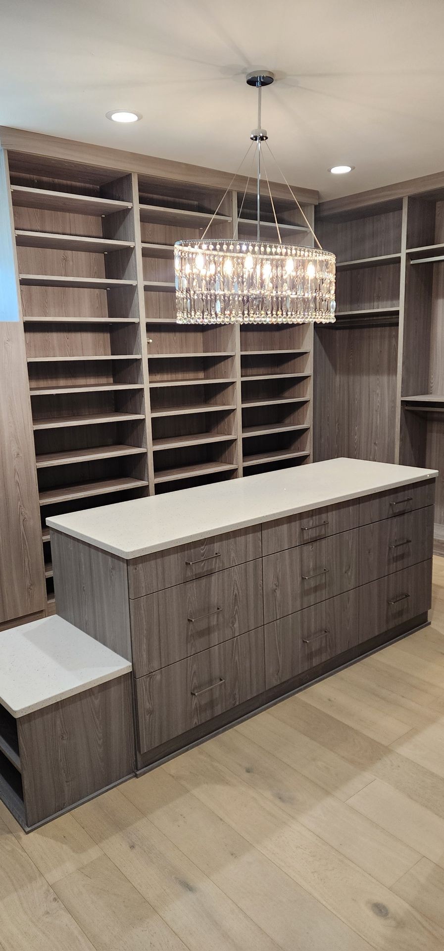 Modern walk-in closet with wooden shelves, a central island, and a crystal chandelier.